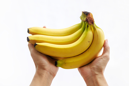 A close-up of hands holding a bunch of bananas against a white background.