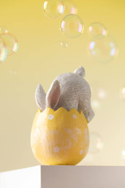 The Easter bunny hid in an egg on a yellow background with flying soap bubbles. The concept of a happy Easter. A holiday card.