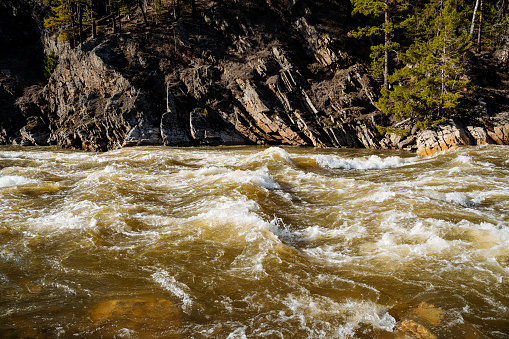 A powerful threshold on a mountain river, the water is bubbling in the channel, the steep rock breaks off into the water, the flow of muddy water, flooding, Aigir Bashkortostan Russia