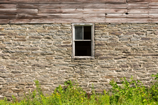 A window in the stone foundation of an old, weathered barn.