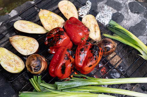 Leeks, whole charred red peppers, aubergines and onions being grilled on a traditional portuguese public asado barbecue.