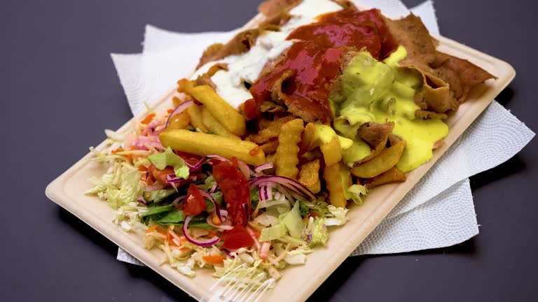 Spicy meat with fries and vegetables with sauce close up on paper eco plate with street food on table with napkins