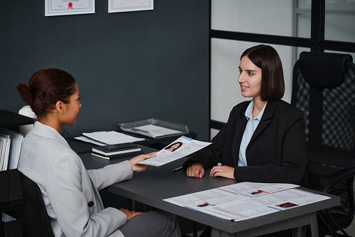 Woman giving her documents to apply visa during interview with specialist in office