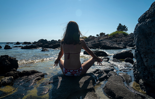 Woman sitting in a yoga pose with legs crossed and meditating at a beach