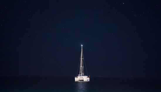 Single white ship sailing on dark black sea at night