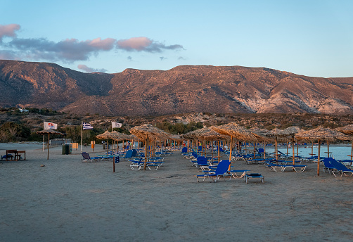 Empty beach resort at dusk. Straw parasols and tall mountains in background