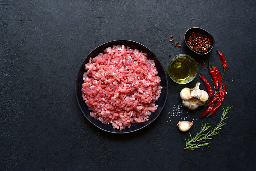 Homemade minced meat with spices on a black slate, stone or concrete background. Top view with copy space.