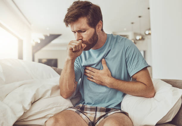 Chory, kaszlący i mężczyzna na kanapie z bólem w klatce piersiowej, gruźlicą lub grypą w domu. Astma, lęk i mężczyzna z problemami z oddychaniem w salonie z covidem, zapaleniem płuc lub wirusem płuc – zdjęcie