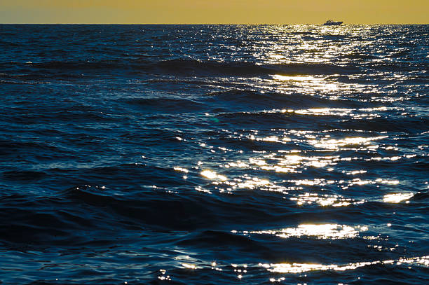 Solitary motorboat cruising the sea at sunset Highlights of reflected sunlight on the waves. One motorboat, distant, cruising on the horizon under the sun. baluginio stock pictures, royalty-free photos & images