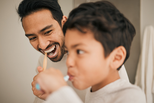 Face of dad, boy and child brushing teeth for hygiene, morning routine or teaching healthy oral habits at home. Happy father, kid and dental cleaning in bathroom with toothbrush, fresh breath or care