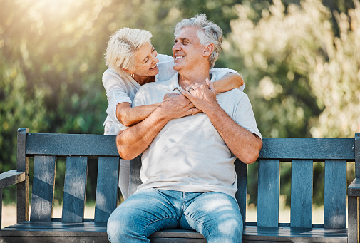 Happy couple, senior and hug on park bench for love, support and bonding together in retirement and nature garden. Smile, relax and elderly woman embrace man in Australia backyard for marriage trust