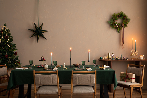 Interior design of christmas dinning room interior with table, christmas tree,  stylish chair, wreath, candle with candle stick, wooden console and personal accessories. Home decor. Template.