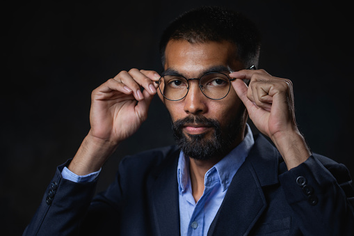Portrait, A bearded man wearing glasses and black suit poses in the studio.