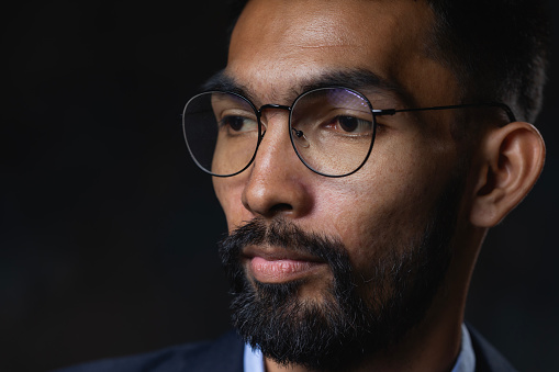 Close-up shot of bearded young man wearing glasses on a black background.