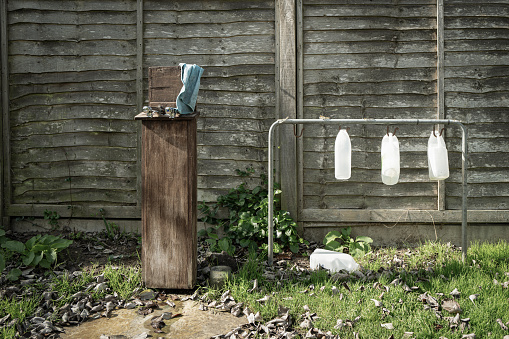 Trio of empty milk cartons used as watering cans for cemetery flowers. An outside tap is on the left.