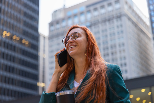 A red-haired businesswoman walking in downtown Chicago, talking on her cell phone.