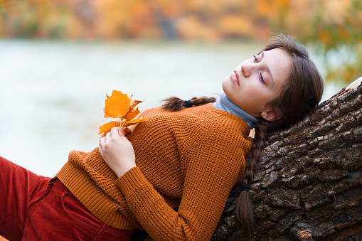 a young teenage girl posing in an autumn forest, lying on a tree, by the riverbank, enjoying the beautiful nature and bright yellow leaves