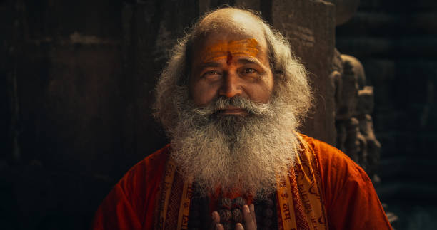 портрет старшего индуистского монаха, смотрящего в камеру и улыбающегося в древнем храме. дружелюбный индийский пожилой мужчина, выдающий  - buddhism monk book zen like стоковые фото и изображения