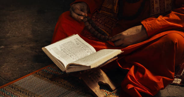 портрет старого индийского монаха, читающего книгу в древнем храме. старший гуру получает мудрость из священных текстов, смиренно читает с� - buddhism monk book zen like стоковые фото и изображения
