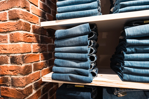 Stacks of blue denim pants are neatly laid out on a shelf in the store. The color of denim pants is blue. Pants differ in different styles and styles to meet the needs of customers with different tastes and preferences.