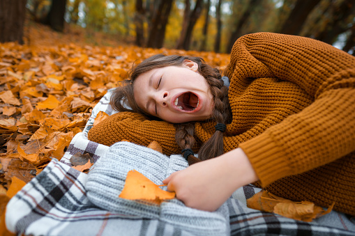 a young teenage girl lies in a clearing by the river bank in the autumn forest, wants to sleep and yawns, enjoying the beautiful nature and bright yellow leaves,