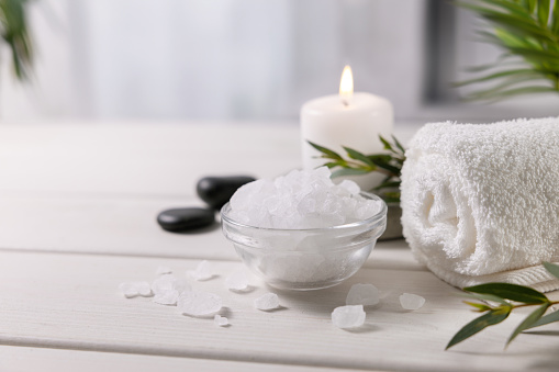 composition with sea salt, towel and candle on white wooden table at spa centre. copy space