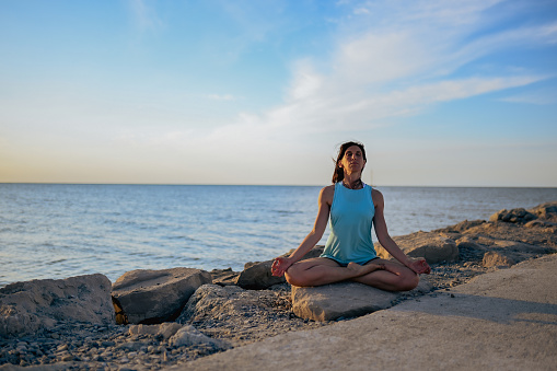 full length portrait of a woman in a lotus position on a beach.