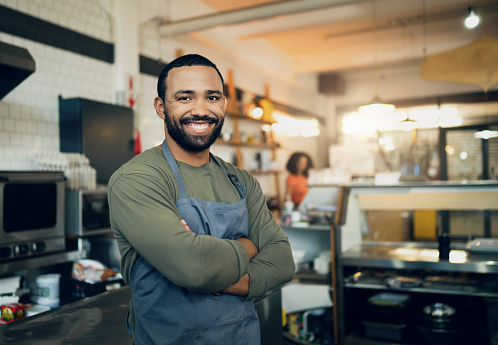 Happy man, portrait and small business owner in kitchen at restaurant for hospitality service, cooking or food. Face of male person, employee or waiter smile in confidence for professional culinary