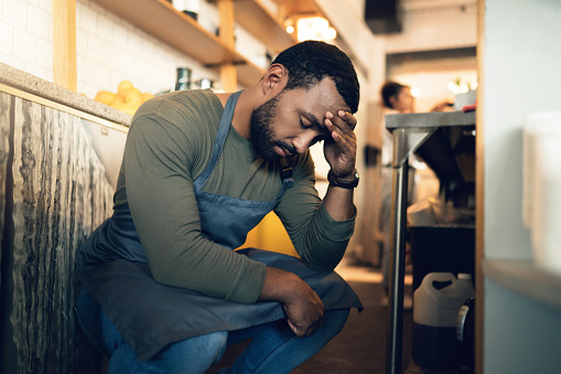 Waiter man, coffee shop and tired with stress, headache or regret for mistake, fail or fatigue at job. Barista person, burnout and pain in head with anxiety, mental health or depression in restaurant