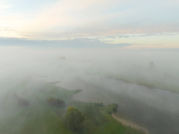 River IJssel covered in a blanket of mist seen from above during a fall morning near the river IJssel in Overijssel. The treetops are popping out over the thick fog with some of the trees starting to change color during the annual autumn season. The fog is giving the landscape a mystical atmosphere.