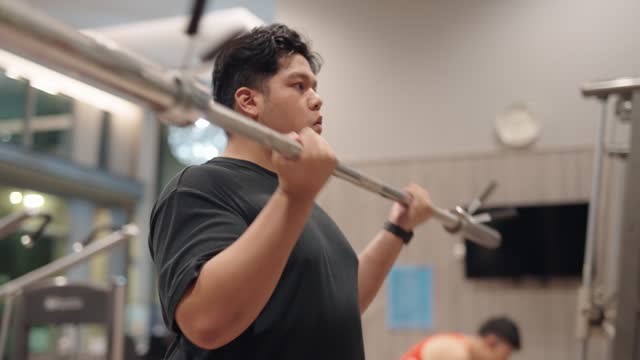An overweight man uses weightlifting for training at a gym