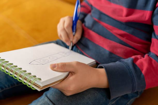 istock a boy concentrating on drawing in his notebook. He clutches the pen in his hand 1767148372