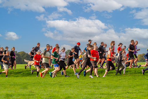 Harrogate, North Yorkshire, UK - September 30, 2023.  A group of people from different ages and abilities running together at a UK Parkrun event in the UK with blue sky and copy space above