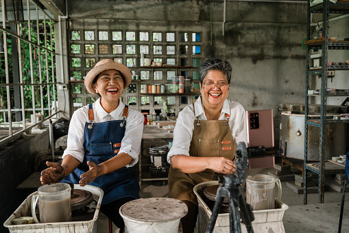 Two Asian senior women friends enjoy  Pottery Classes while live streaming on smart phone.