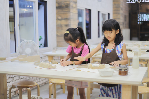 Two Asian girls kneading clay in the pottery classroom,  they wearing aprons to prevent their clothes from getting dirty