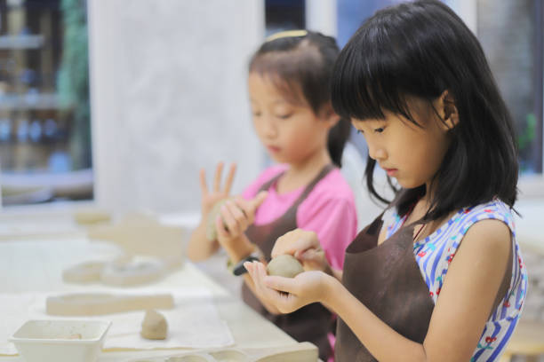 Two Asian girls kneading clay in the pottery classroom,  they wearing aprons to prevent their clothes from getting dirty
