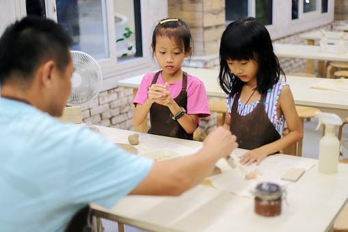 An Asian father accompanies his two daughters to knead clay with their hands. The actual experience is an activity that is highly valued in education nowadays.