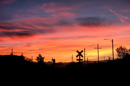 Railroad crossing under bright orange, purple and pink clouds at sunset