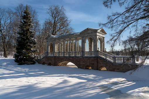 Marble bridge on the shore of a Large pond in the Catherine Park in Tsarskoye Selo on a sunny winter day, Pushkin, St. Petersburg, Russia