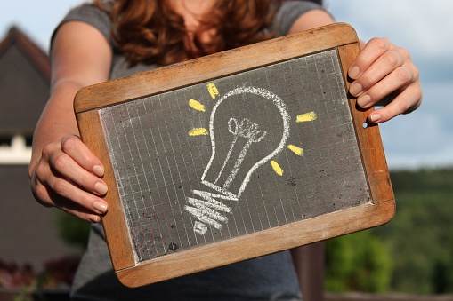 lightbulb (idea) sketched with chalk on slate shown by young female
