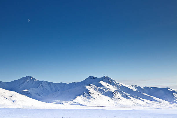 Chandalar Shelf and crescent moon over snow-covered Brooks Range mountains in winter, Alaska.