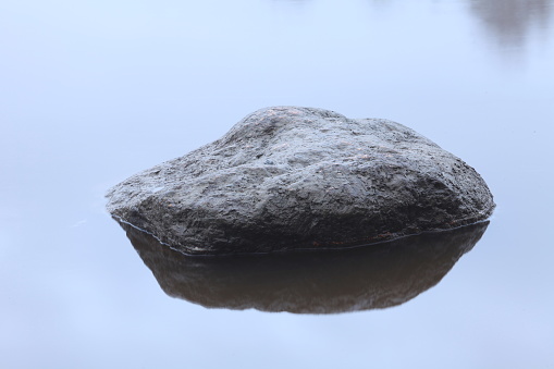 large smooth boulder rises above the surface of the river and is reflected in the mirror water