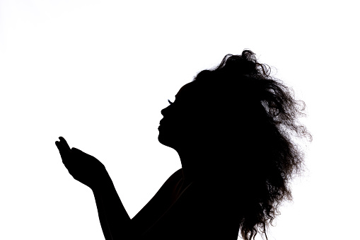 A silhouette of a woman with big hair against a white backdrop reaching with her hands in front of her