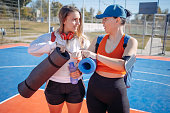 Young woman going on exercise class with a friend holding exercise mat in hand