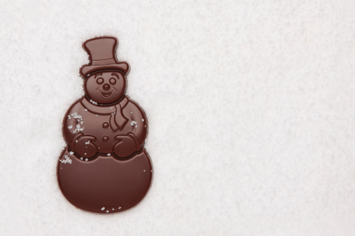 Chocolates snowman on the snow background. Copy space.