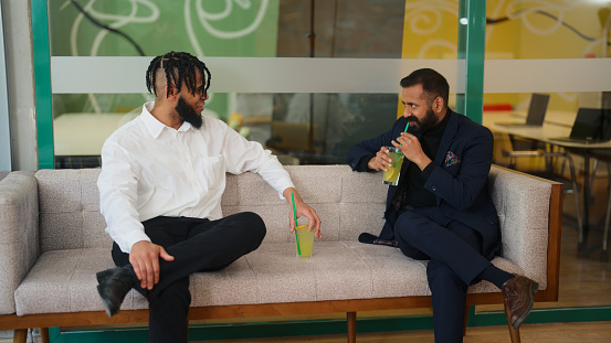 Two businessmen are causally talking with each other in a modern co-working office.