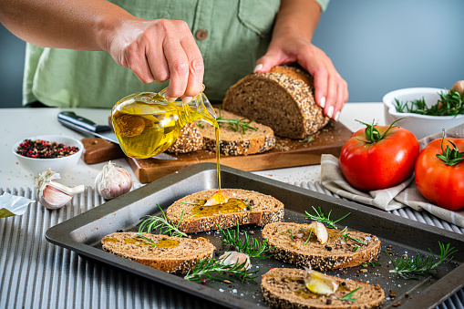 Woman pouring olive oil on slices of bread in a baking sheet