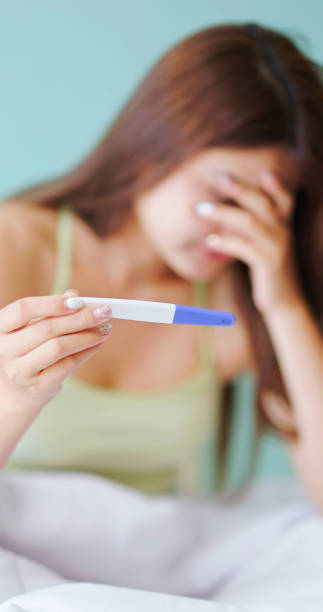 women has pregnancy test asian depressed woman is looking at her pregnancy test at home and she pregnant out of wedlock unusual couple stock pictures, royalty-free photos & images