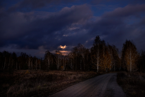 Full moon in the clouds and a road in the autumn forest. Night photo.