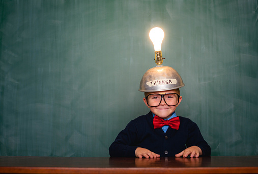 A young nerd boy has a bright idea with copy space in front of a chalkboard. His lightbulb helmet helps him think of the next big idea.